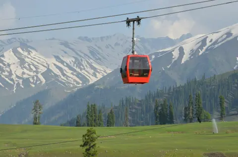 A red gondola cabin rising over the Gulmarg meadows